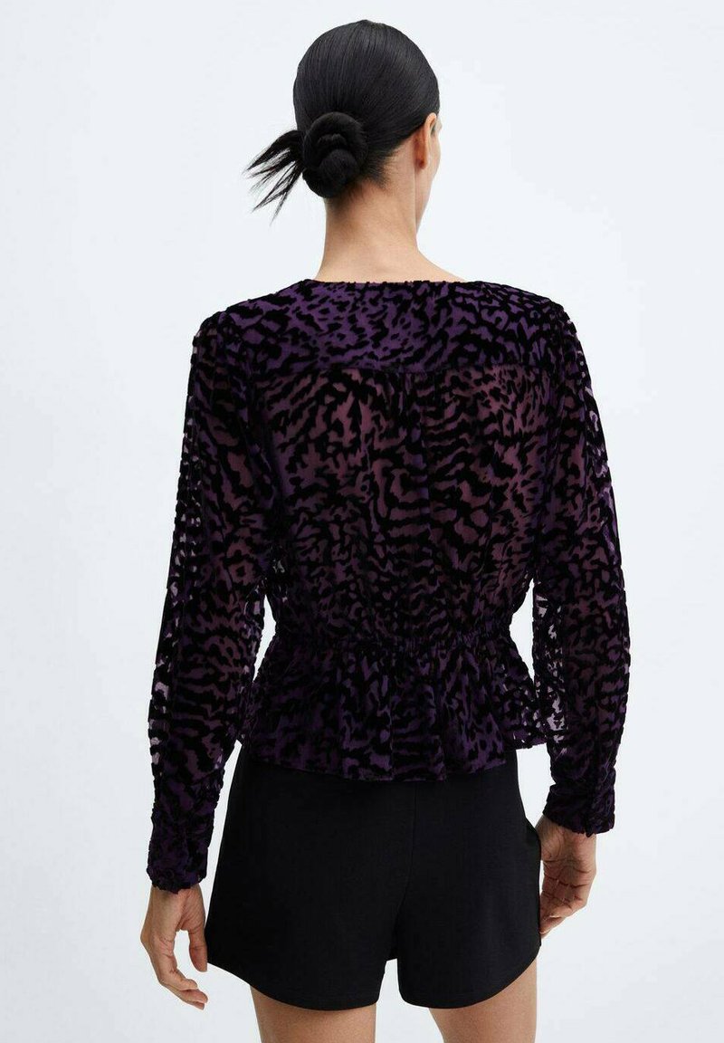 Top de terciopelo morado de manga larga con diseño peplum, cintura fruncida y patrón de leopardo, combinado con pantalones cortos negros.
