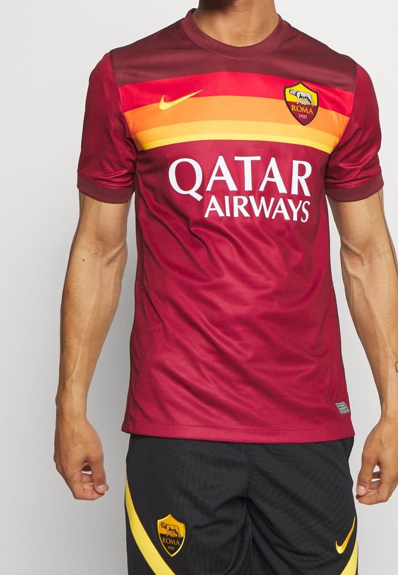 Personne portant un maillot de football rouge de l'AS Roma avec des bandes jaunes et orange et le logo Qatar Airways, ainsi qu'un short noir orné de l'écusson de l'AS Roma.