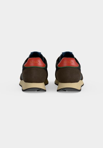 Paire de baskets marron et beige avec des languettes rouges au talon et des semelles noires, vues de dos sur un fond uni gris clair.