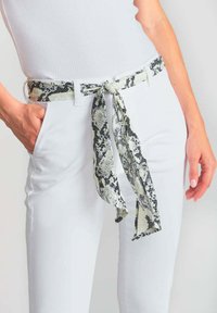 Weißer Gürtel mit einem Schlangenmuster in Schwarz und Grau, in einer Schleife um die Taille gebunden, mit glatter Textur und leichtem Material.