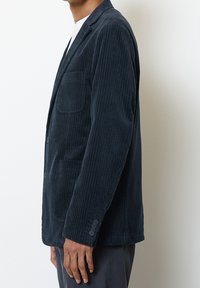 Blazer in corduroy blu Navy con revers a punta, tasche frontali e polsini a tre bottoni. Texture a coste verticali, vestibilità sartoriale.