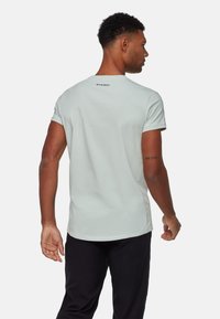 Chemise verte clair à manches courtes avec col rond et logo au dos. Texture lisse, design ajusté, associée à un pantalon noir.