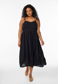 Zwarte maxi-jurk met dunne bandjes, aansluitend bovenstuk en geraffineerde taille, gemaakt van lichte stof. Getextureerde instap schoenen.