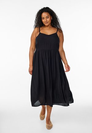 Black maxi dress with thin straps, fitted bodice, and gathered waistline, made from lightweight fabric. Textured slip-on shoes.