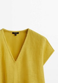 Top jaune en lin à manches courtes avec un profond col en V et des détails aux bords francs sur l'encolure, présenté sur fond blanc.