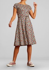 Tištěné šaty s přiléhavým tělem, rozšířenou sukní a krátkými rukávy. Tkanina vykazuje barevný vzor listů na krémovém pozadí.