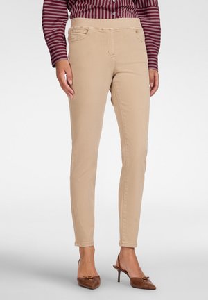 Person trägt beige Slim-Fit-Hosen, braune spitze Absätze und ein langärmeliges bordeauxfarbenes Hemd mit weißen Streifen.