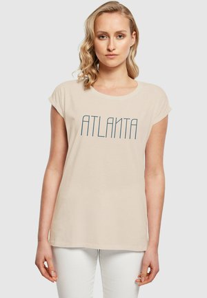 Šviesiai ruda T-marškiniai su trumpomis suktomis rankovėmis ir apvaliu kaklu. Pirmoje pusėje yra žodis "ATLANTA" tamsiai mėlynos spalvos vertikaliu šriftu.