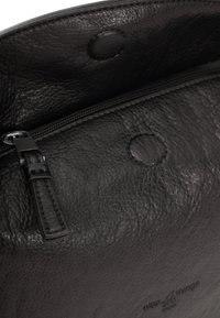 Interno di una borsa in pelle nera con chiusura a zip, superficie testurizzata e dettaglio a forma di bottone circolare. Etichetta visibile vicino al fondo.