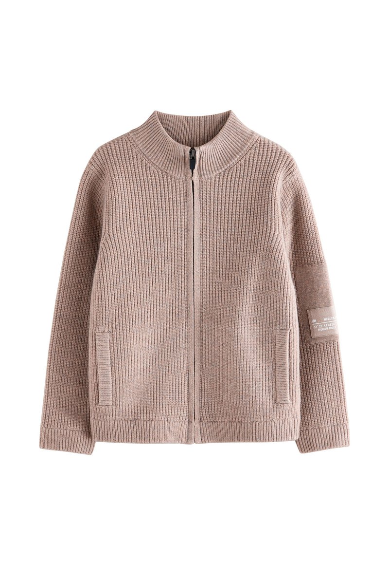 Suéter de punto en marrón claro con cuello alto, cierre frontal completo con cremallera, bolsillos laterales, textura acanalada y un detalle de parche en la manga izquierda.