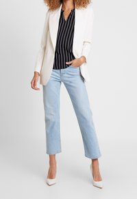 Vit skräddarsydd kavaj över en svart vertikalt randig blus, matchad med ljusblå raka jeans och vita högklackade skor.