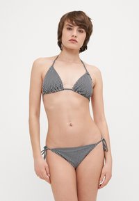Stripet svart og hvit bikini med trekantet topp og knyting i sidene. Laget av glatt stoff, med tynne stropper og minimalistisk design.