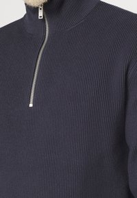 Granatowy prążkowany sweter z wysokim kołnierzem i zamkiem na pół, wykonany z strukturalnej tkaniny zapewniającej ciepło i smukły design.