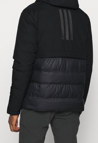 Svart pufferjacka med huva, med en horisontell quiltad design, slät textur och tre vertikala ränder på baksidan.