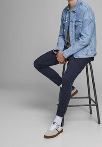 Ljust blå denimjacka över en grårandig skjorta, tillsammans med mörka cargobyxor och vita sneakers med bruna sulor. Reagerar främst på form och färg.