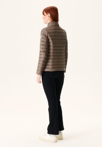 Bruine, puffy gewatteerde jas met horizontale stiksels, hoge kraag en logodetail op de schouder, gecombineerd met zwarte flared broeken en witte sneakers.