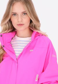 Světl růžová voděodolná bunda s ukrytým zipem, nastavitelnou kapucí a stříbrnými logo akcenty. Nositelná přes pruhované tričko.