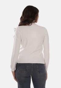 Maglione grigio chiaro, tessuto lavorato a maglia con un sottile luccichio, design aderente, maniche lunghe, orlo a costine, abbinato a jeans skinny scuri.