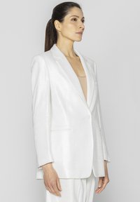 Biały żakiet wykonany z lekkiego materiału, z pojedynczym guzikiem, klapami w kształcie notcha oraz dwiema przednimi kieszeniami o gładkiej fakturze.