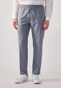 Grau karierte Hose mit einem elastischen Bund, Kordelzugverschluss und lässiger Passform, kombiniert mit weißen Sneakers.