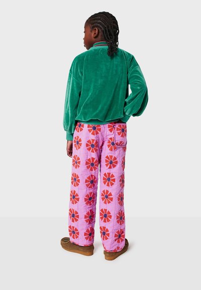 Veste en velours vert avec un col haut, associée à un pantalon rembourré rose présentant un motif floral rouge et bleu marine. Des chaussures marron complètent l'ensemble.