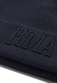 Merinoknitted beanie sininen, pehmeä tekstuuri, jossa on tummansinisellä brodeerattu "PUMA"-logo. Kangas on venyvää ja lämmintä.
