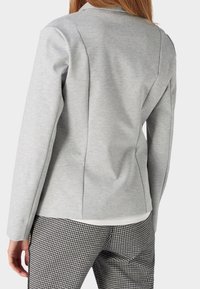 Jasnoszary żakiet o dopasowanym kroju, z wyraźnymi liniami, długimi rękawami i miękkim materiałem, zestawiony z spodniami w czarno-białą kratę houndstooth.