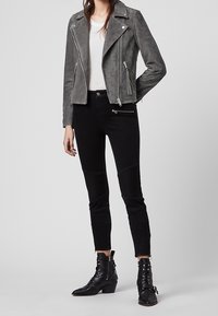 Šedá semišová motorkářská bunda se zipovými kapsami, v kombinaci s černými skinny džíny s prošívanými detaily a černými kotníkovými botami.