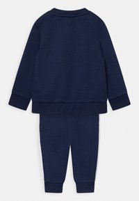 Set de sudor și pantaloni de culoare bleumarin, realizat dintr-un material moale, cu manșete ribbate și o bândă albă pe laturile pantalonilor.