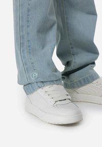 Lichtblauwe denimjeans met een relaxte pasvorm, voorzien van een subtiele geborduurde logo en gecombineerd met witte sneakers met textuuraccenten.