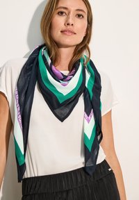 Foulard in seta con un motivo geometrico nei toni del blu navy, verde e viola. Indossato in modo leggero attorno al collo, ha una consistenza leggera e trasparente.