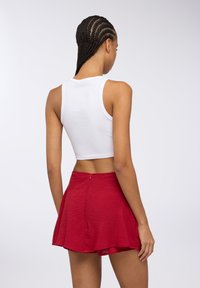 Top corto bianco abbinato a una mini gonna rossa con texture, dotata di chiusura con zip sul retro. Tessuto liscio con motivi sottili.