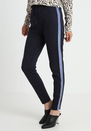 Navy slim-fit broeken met blauw-witte gestreepte zijpanelen, elastische tailleband en zachte stof; gecombineerd met zwarte hoge muiltjes.