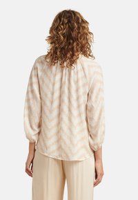 Lightweight blouse in pale cream with a chevron pattern in soft beige. Features puffed sleeves and a gathered yoke for added texture.