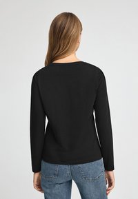 Svart långärmad topp med rund halsringning, slät textur och figursydd passform. Matchad med blå jeans med bakfickor.