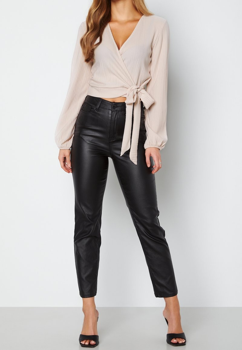 Haut enroulé beige avec texture plissée et manches longues, associé à un pantalon en cuir noir ajusté et des talons ouverts noirs.