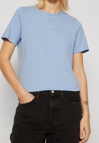 Ljusblå T-shirt i mjukt tyg, med rund halsringning och korta ärmar, med en subtil stitchad logotyp på framsidan.