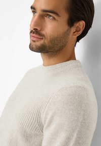 Hellgrauer Strickpullover mit rundem Halsausschnitt und geripptem Muster. Weiches Material mit subtilen Farbvariationen. Lässige Passform, präsentiert an einem Model.