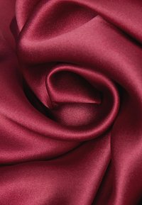 Tejido satinado burdeos, suave y brillante, presenta un acabado lustroso con pliegues caídos que crean una textura suave y fluida.