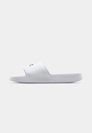 Witte slidesandaal met een brede band met een groen logo. Glad synthetisch materiaal, platte zool en een minimalistisch ontwerp.