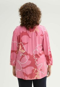 Blouse florale rose à manches longues, présentant un contour blanc de grandes fleurs dans des nuances variées de rose et un tissu lisse et léger.