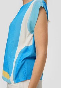 Blaues Kurzarmoberteil mit abstrakten weißen und gelben Mustern, glatter Textur, lockerer Passform und rundem Ausschnitt.