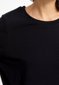 Czarna krótkozbrodowa koszulka o okrągłym dekolcie, wykonana z gładkiego, lekkiego materiału, cechująca się prostym i jednolitym wzornictwem.