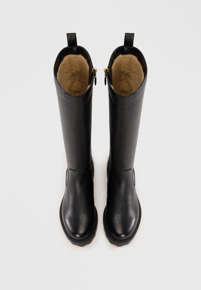 Bottes noires en cuir grand format avec une finition texturée, intérieur beige doublé et accents de fermeture éclair dorés sur le côté. Design de bout rond lisse.