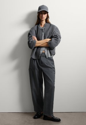 Gray wool bomber jacket with fitted cuffs, layered over a gray top, paired with loose gray trousers and black loafers, complemented by a cap.