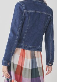 Ciemnoniebieska kurtka z denimu o dopasowanym kroju, z mankietami na guziki i kontrastowym przeszyciem, noszona na wielokolorowej kratkowanej spódnicy.