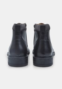 Stivali alla caviglia in pelle nera con tomaia in camoscio, chiusura con cerniera laterale e suola in gomma. Presentano una finitura testurizzata e un design minimalista.