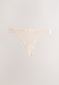 Chiloți tip tanga din bumbac bej deschis, cu o fundiță decorativă mică în față, în centru, pe un fundal simplu, deschis.