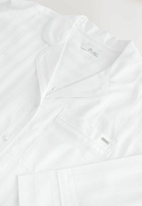 Weißes Pyjama-Oberteil mit Reverskragen, Brusttasche und sichtbarem Next Studio-Label im Halsausschnitt.