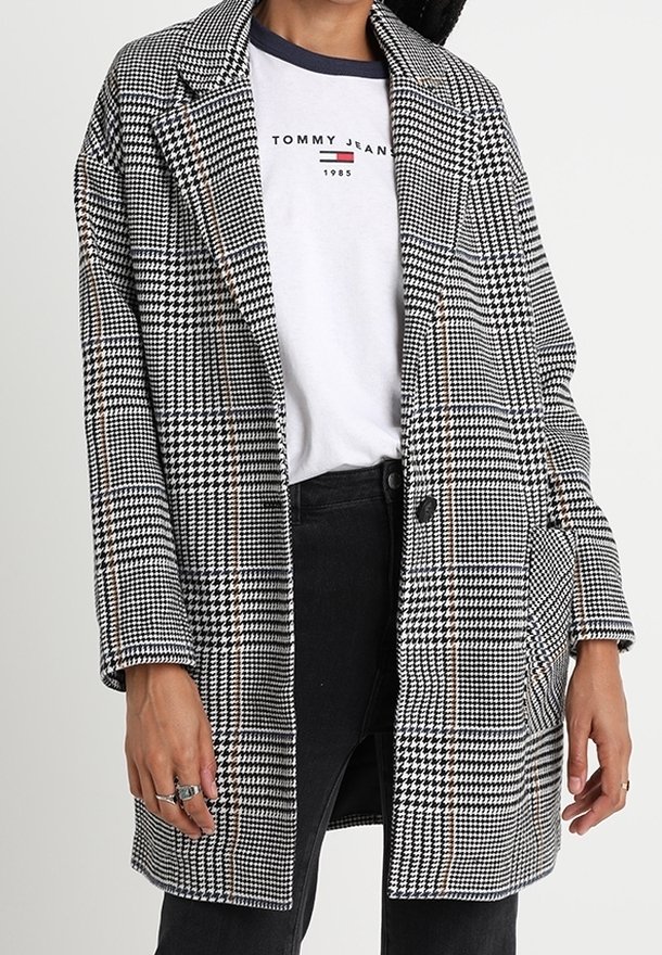 Svart- och vitrutigt kavaj med notched krage, oversize passform, enkel knappstängning och texturerat tyg. Lager på en vit T-shirt.